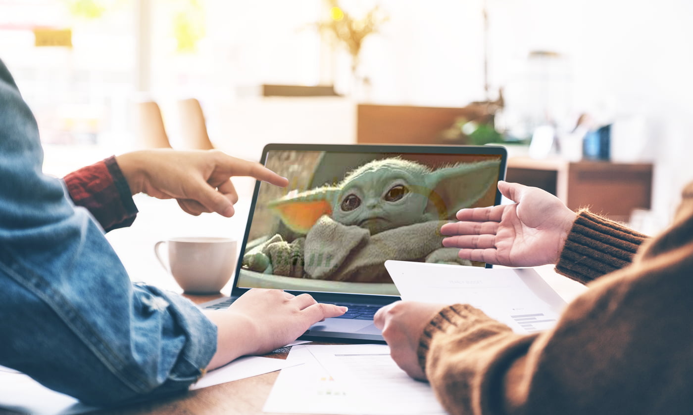 two people collaborating while pointing at laptop with picture of baby yoda on it